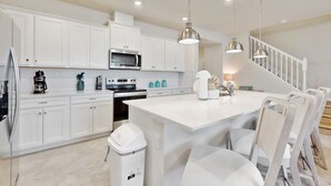 Une cuisine moderne avec des meubles blancs, des appareils en acier inoxydable et des luminaires suspendus.