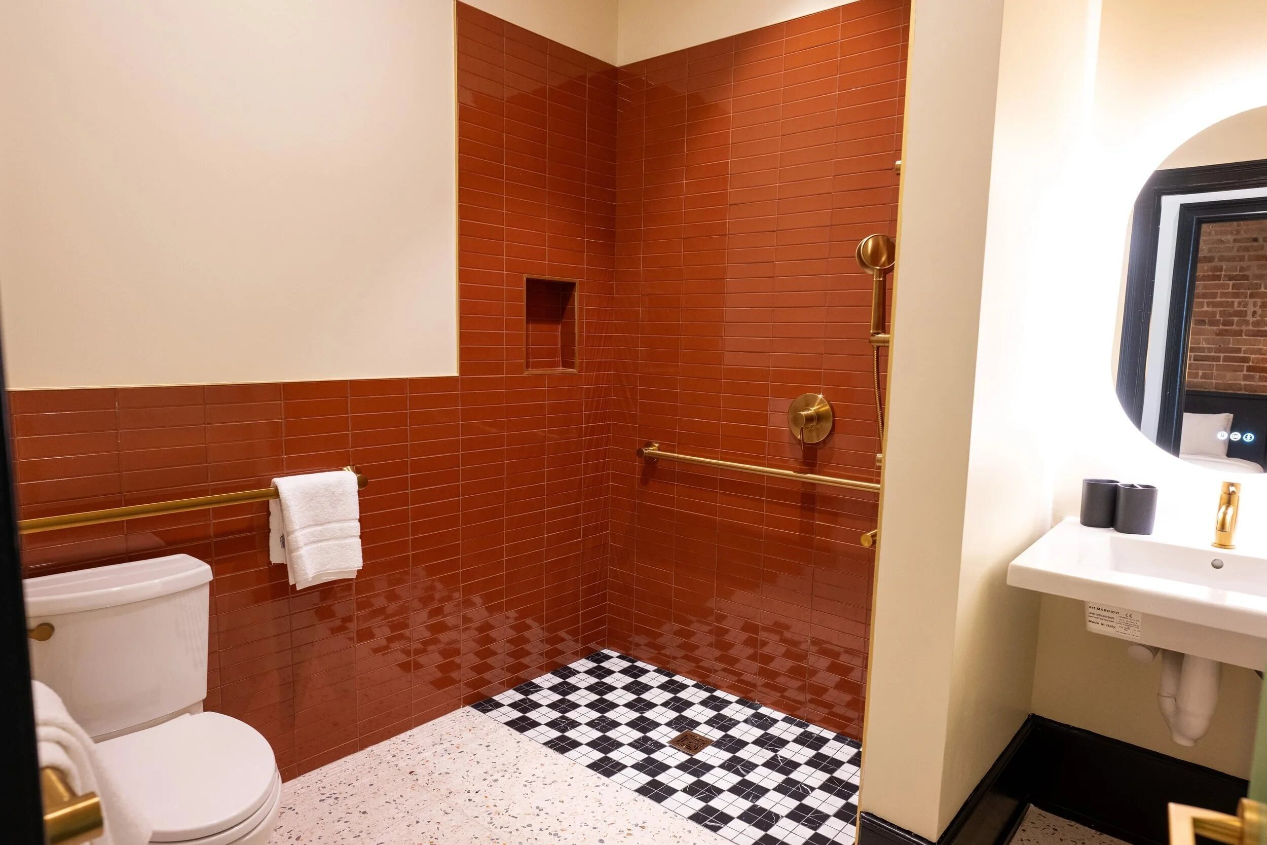 A bathroom with a checkered floor, a white toilet, a sink with a mirror, and a shower area with red tiles.