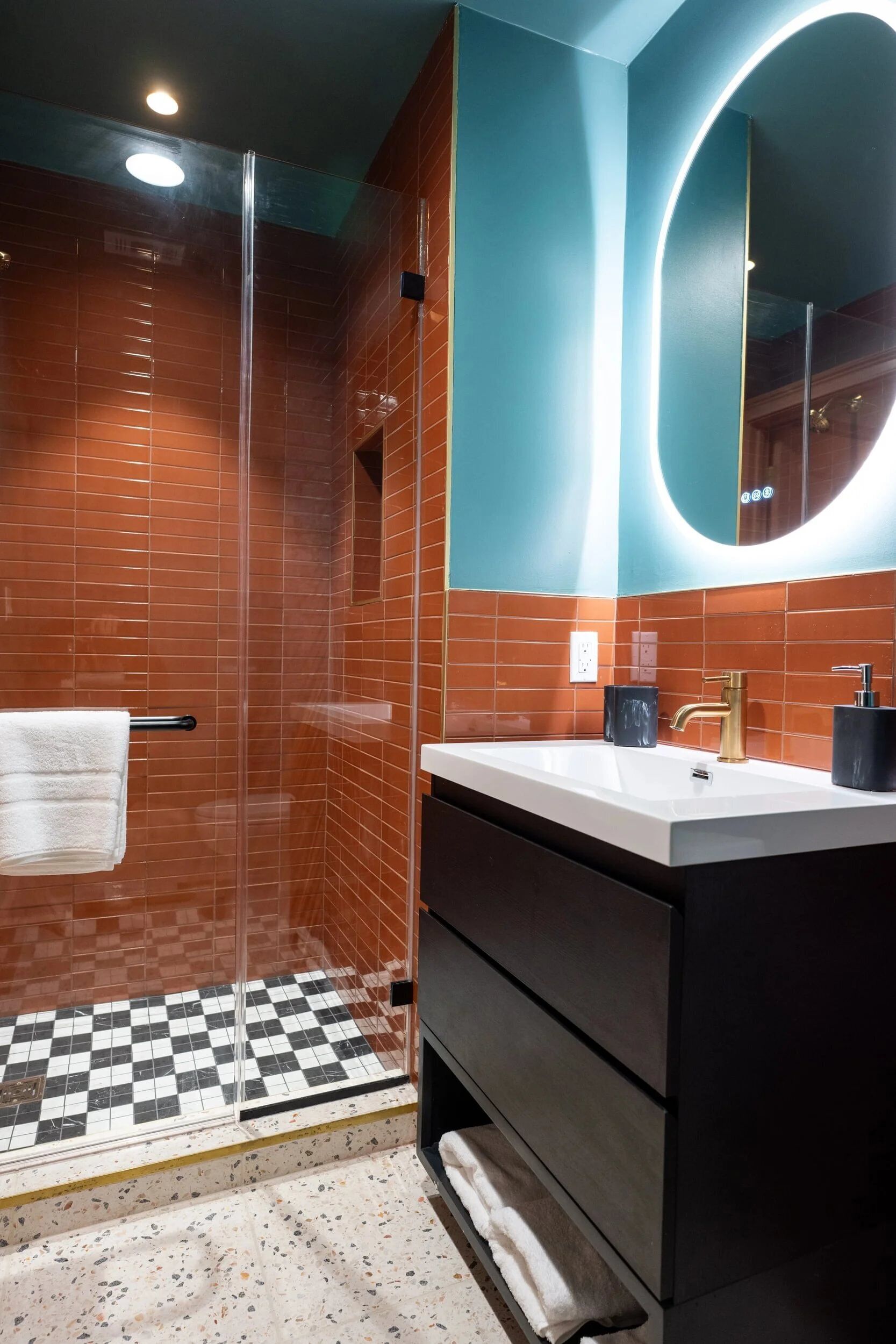Ein modernes Badezimmer mit einer gläsernen Duschkabine, einem weißen Waschbecken mit Goldarmatur und einem großen Spiegel über der Waschtischablage.