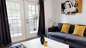 Un salon avec un canapé gris, des coussins jaunes, une table basse blanche et un tableau accroché au mur.