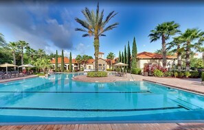 A large outdoor swimming pool surrounded by palm trees and cypress trees, with lounge chairs and umbrellas. - Resort condo with heated pool, gym, BBQ area, patio, W/D, children's pool, AC (Davenport)