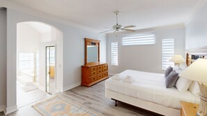 Un dormitorio con cama, cómoda, espejo, ventilador de techo y vistas a través de una puerta abierta.