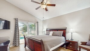 Un dormitorio con cama de madera, una mesita de noche, una silla, un ventilador de techo y una ventana con cortinas.