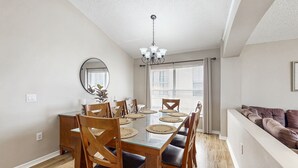 Comedor con mesa de vidrio, sillas de madera y una lámpara de araña.