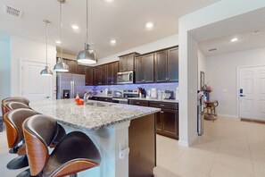A modern kitchen with dark wood cabinets, a granite countertop, and stainless steel appliances. There are three pendant lights, a built-in oven, and a refrigerator. - Charming Davenport house: Dog-friendly, pool, patio, well-equipped kitchen (Davenport)