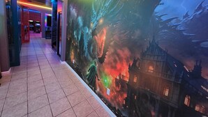 Passadís amb un mural d'un drac i un castell, sòl de rajoles i il·luminació LED colorida.