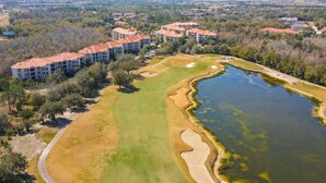 An aerial view of a golf course with a water body, surrounded by residential buildings with red roofs. - Resort condo with heated pool, gym, BBQ area, balcony, W/D, children's pool, AC (Davenport)