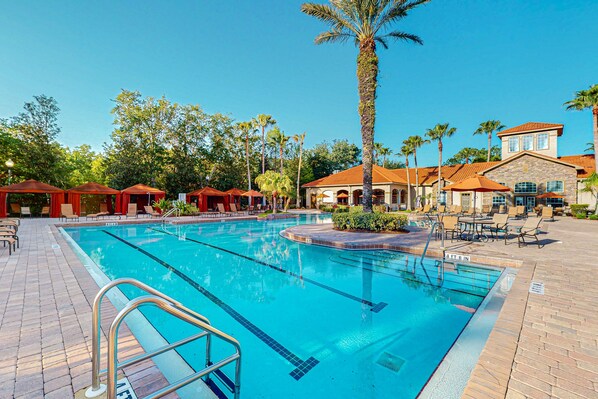A swimming pool with a tiled deck, palm trees, and outdoor seating areas. - Resort condo with heated pool, gym, BBQ area, balcony, W/D, children's pool, AC (Davenport)