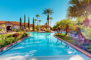 A swimming pool with a tiled deck, surrounded by palm trees and a building with a red-tiled roof. - Resort condo with heated pool, gym, BBQ area, balcony, W/D, children's pool, AC (Davenport)