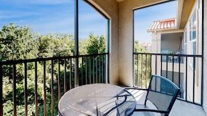A balcony with a round table and chairs, large windows, and a view of trees and buildings. - Resort condo with heated pool, gym, BBQ area, balcony, W/D, children's pool, AC (Davenport)