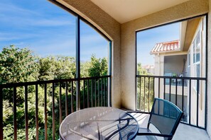 Ein Balkon mit rundem Tisch und Stühlen, großen Fenstern und Blick auf Bäume und Gebäude.