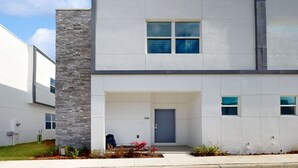 A modern two-story building with a stone facade, a blue door, and a small porch area. - Modern Townhouse with Private Pool Near Disney & Top Attractions (Davenport)