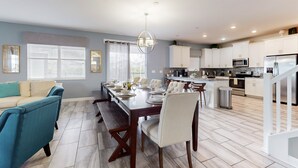 Una cocina moderna con armarios blancos, un comedor con mesa y sillas de madera, y una escalera que lleva a otro nivel.