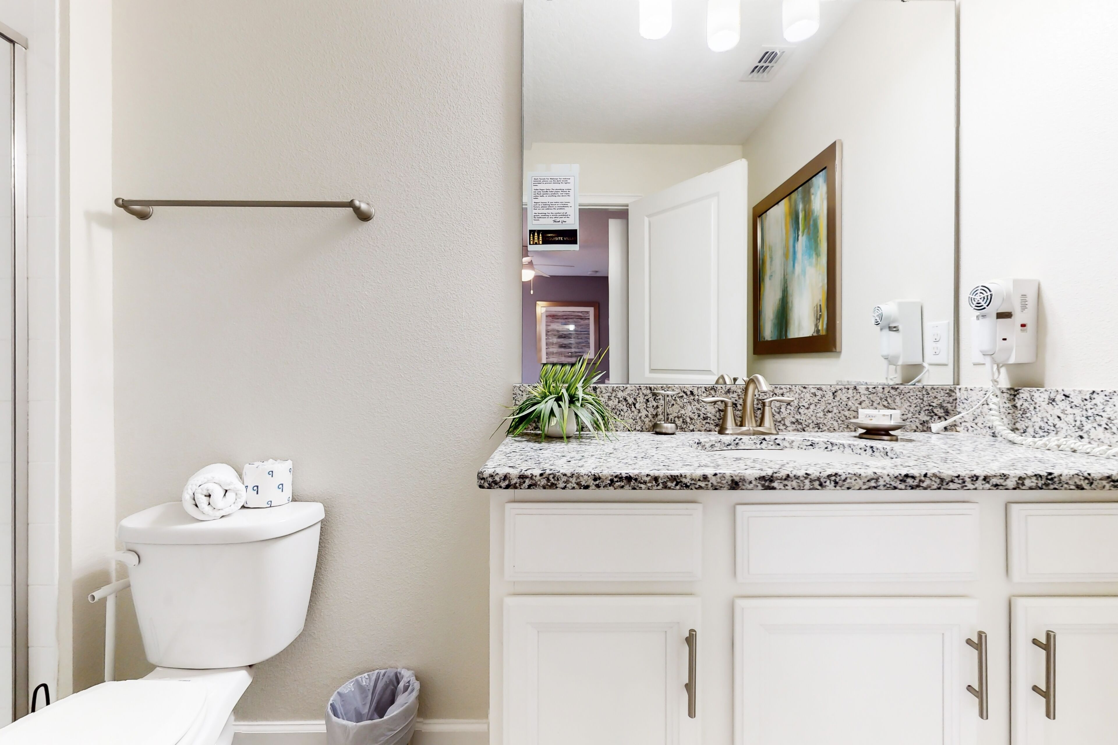A bathroom with a toilet, a towel rack, a sink with a granite countertop, and a mirror.