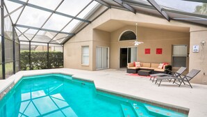 Una piscina exterior cubierta con techo de vidrio, un sofá y dos sillones.