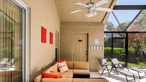 Un patio iluminado por el sol con un sofá color arena, dos sillones de descanso y un ventilador de techo.