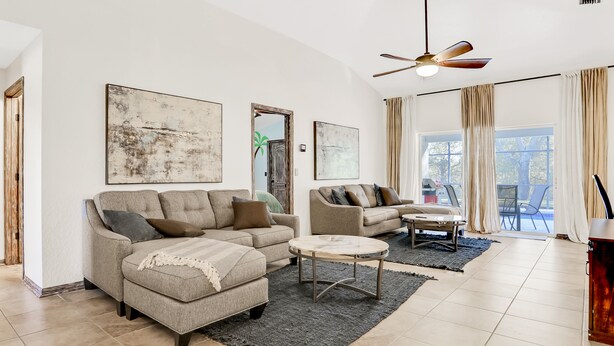 Ein geräumiges Wohnzimmer mit einem großen Sofa, einem kleineren Sofa, einem Couchtisch und einem Deckenventilator.