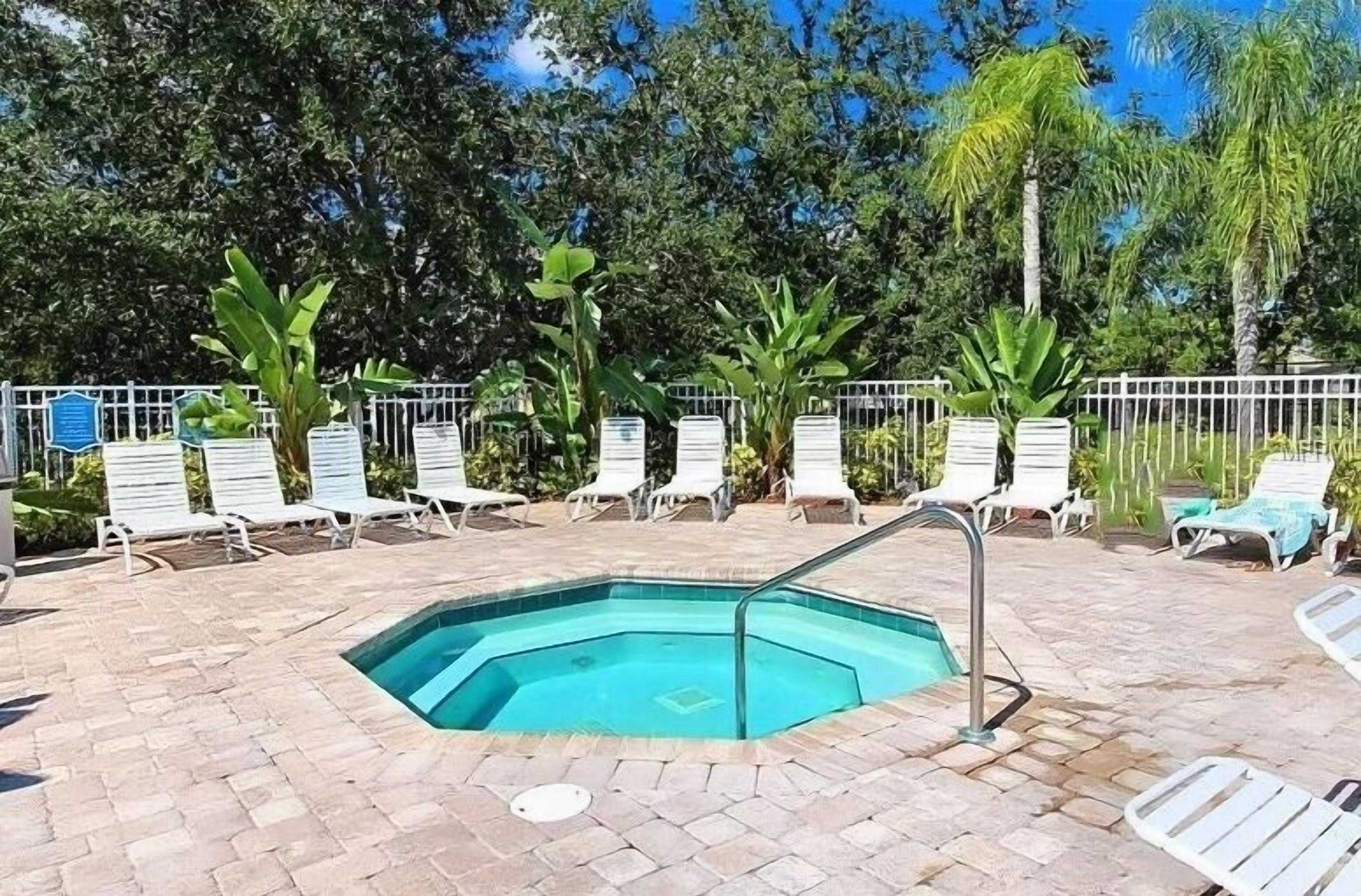 Une piscine dotée d’une terrasse carrelée, entourée de chaises longues blanches et d’une clôture en métal.