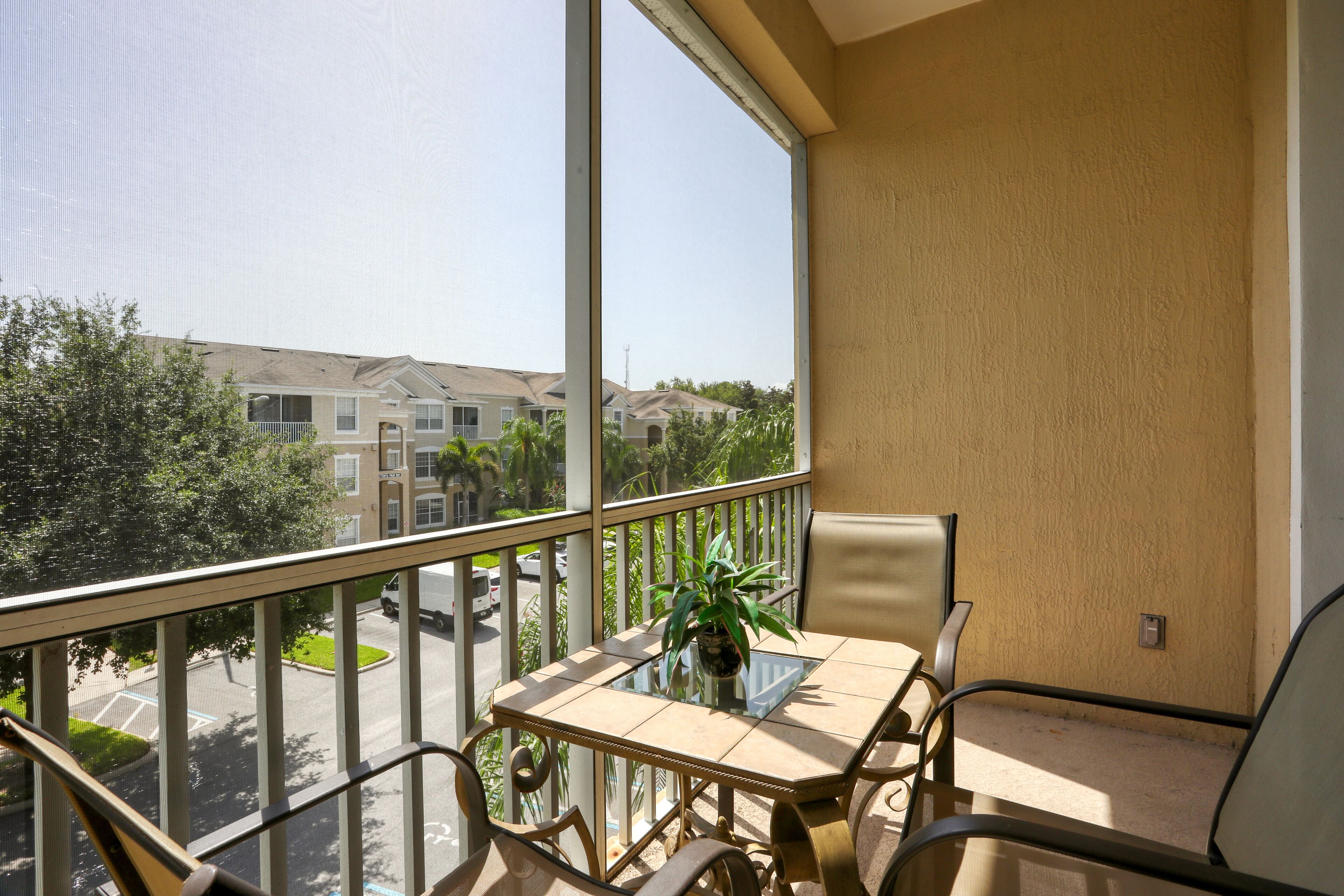 A balcony with a table and chairs, a potted plant, and a view of a residential area.