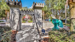 Un arco de estilo castillo con una reja de cadena, rodeado de palmeras y una escultura verde.