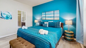 A bedroom with a blue accent wall, a bed with matching pillows, a bedside lamp, and a round side table. - Dog-friendly ground-floor home in gated community w/lake views & enclosed patio (Davenport)