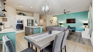 A modern kitchen with white cabinets, a dining area with a table and chairs, a living room with a sofa, and a ceiling fan. - Dog-friendly ground-floor home in gated community w/lake views & enclosed patio (Davenport)