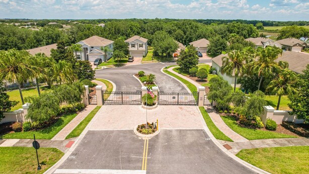 A residential area with houses, a gated entrance, and a central flagpole. - Dog-friendly ground-floor home in gated community w/lake views & enclosed patio (Davenport)