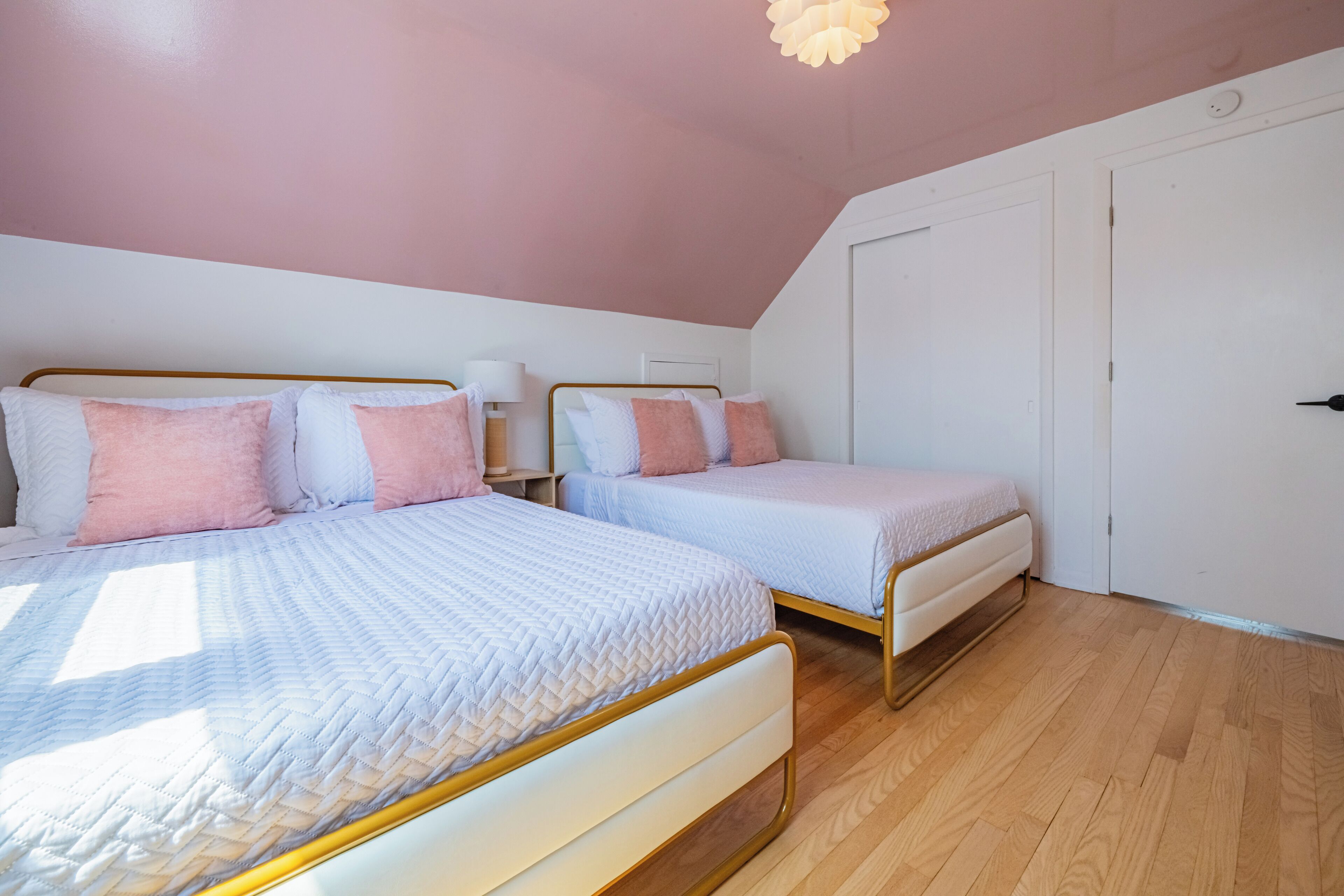 Une chambre avec deux lits, un plancher en bois et un plafond rose.