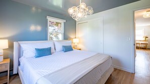 Een slaapkamer met een groot bed, twee nachtkastjes met lampen, een raam met uitzicht en een deur naar een andere kamer.