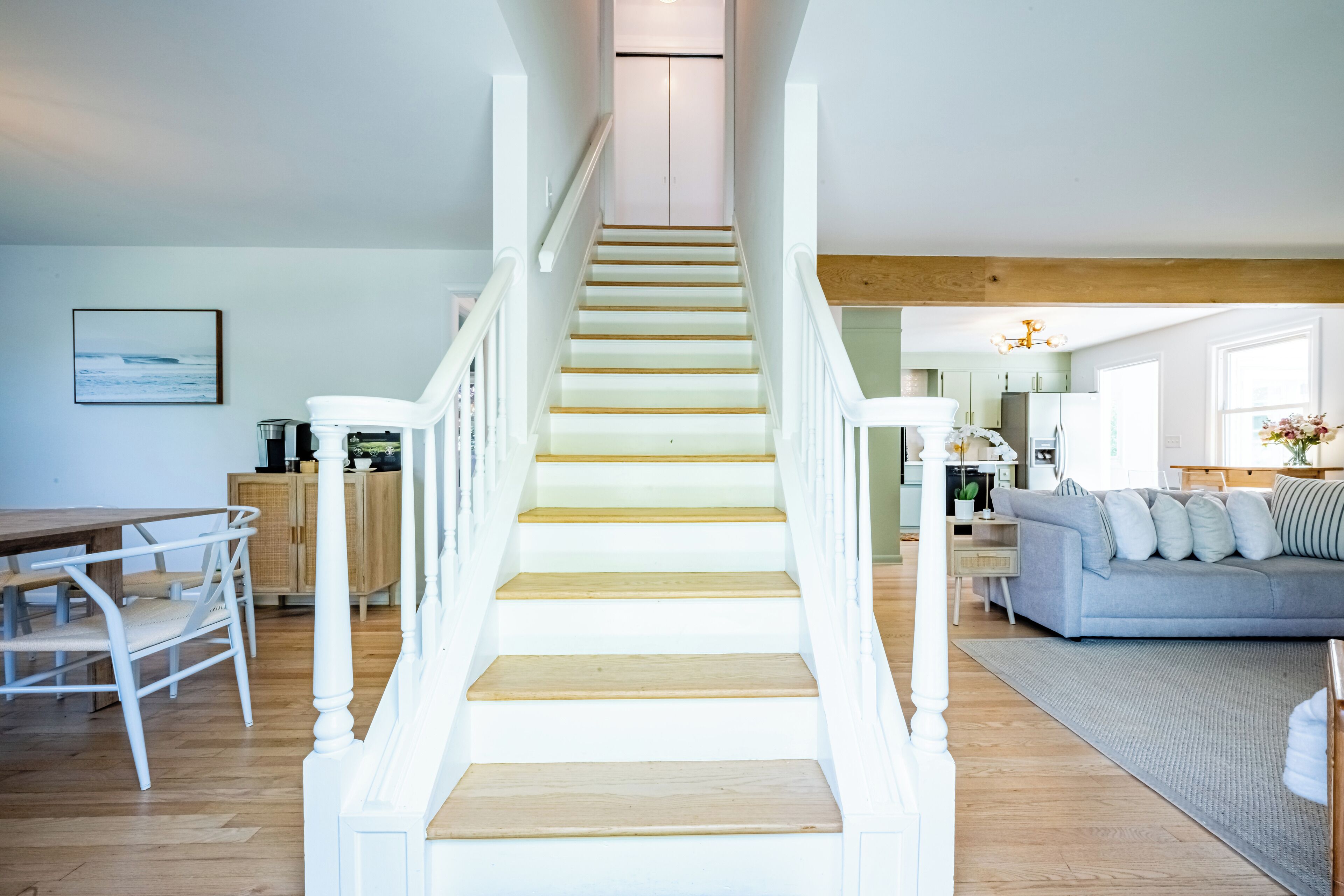 A staircase leading to a living area with a dining table and chairs, a sofa, and a kitchen in the background.
