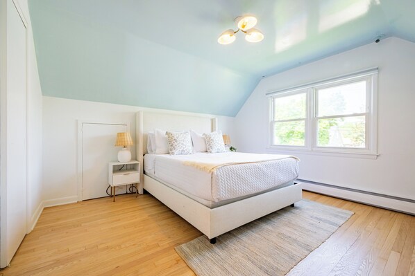A bedroom with a bed, bedside table, lamp, and a large window. - Cozy Cottage with Fire Pit (Fairfield)