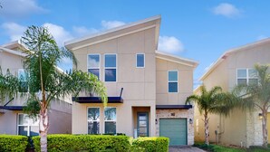 A modern two-story residential building with a green door, a garage, and a well-maintained lawn with palm trees. - Spacious family villa with private pool, spa and movie loft (Kissimmee)