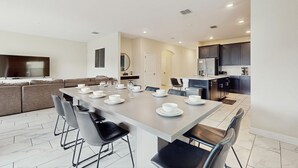 A modern kitchen with dark cabinets, a built-in oven, and a dining area with a long table set for six. - Spacious family villa with private pool, spa and movie loft (Kissimmee)