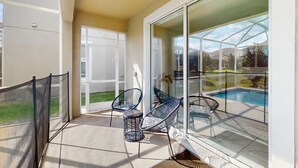A balcony with a glass door leading to a pool area, two chairs, and a small table. - Spacious family villa with private pool, spa and movie loft (Kissimmee)