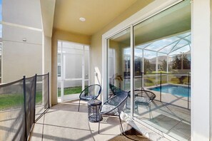 Ein Balkon mit Glastür zum Poolbereich, zwei Stühle und ein kleiner Tisch.