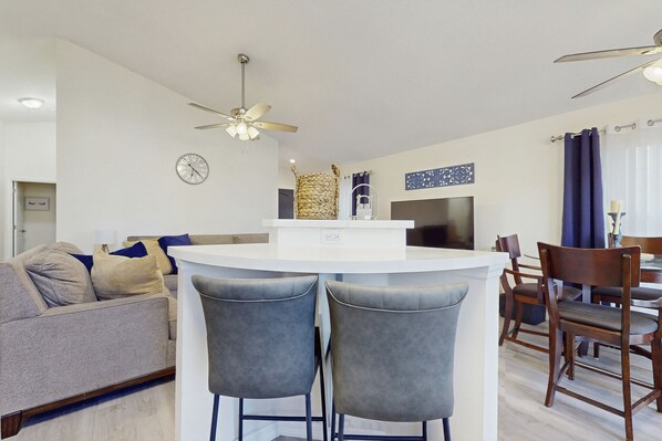 A modern kitchen with a central island, bar stools, a dining area with wooden chairs, and a ceiling fan. - Radiant retreat with private pool,  on-site golf, board games, AC, & W/D (Haines City)