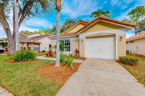 A residential house with a white garage door, a number 2460 garage, and a well-maintained lawn with various plants. - Radiant retreat with private pool,  on-site golf, board games, AC, & W/D (Haines City)