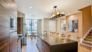 A modern kitchen with wooden cabinetry, a central island, and a dining area with a table and chairs. - Modern villa with patio, grill, central AC, WiFi, shared pool, tennis, & gym (Kissimmee)