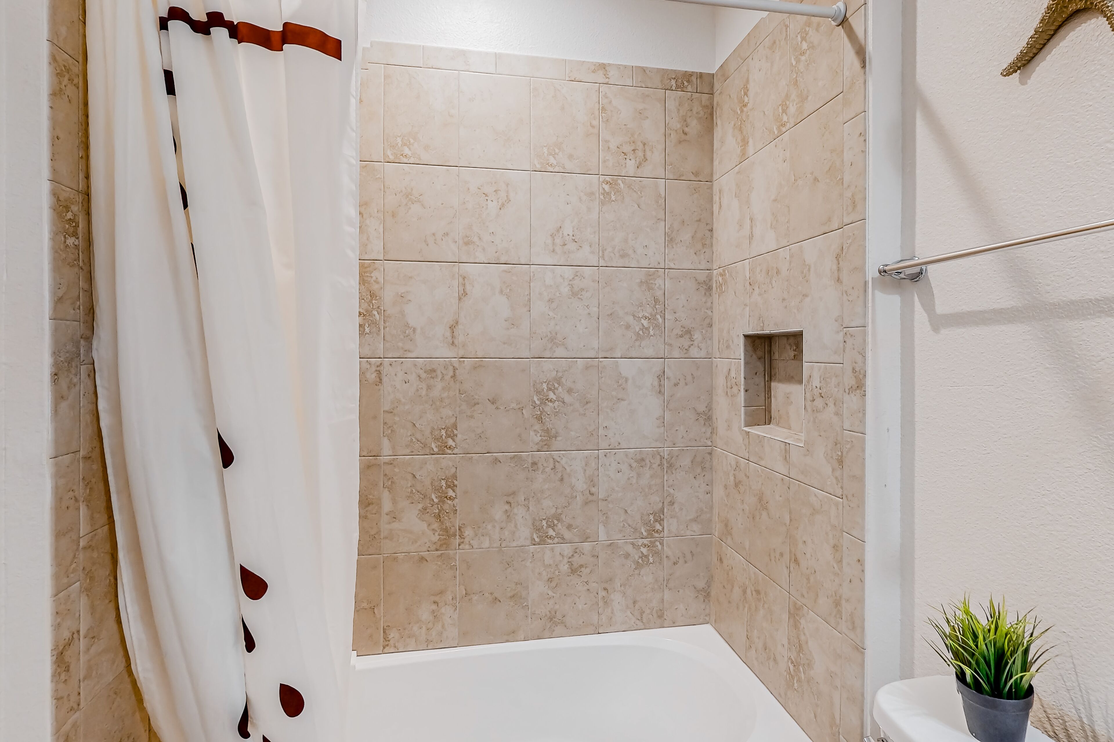 A shower area with beige tiles, a white bathtub, and a potted plant.