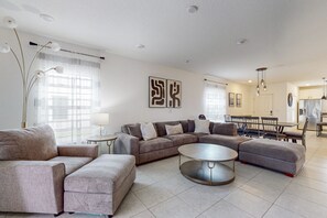 A modern living room with a sectional sofa, a round coffee table, and a dining area with chairs and a table. - Cozy townhouse with private screened patio & community pool – near theme parks (Davenport)