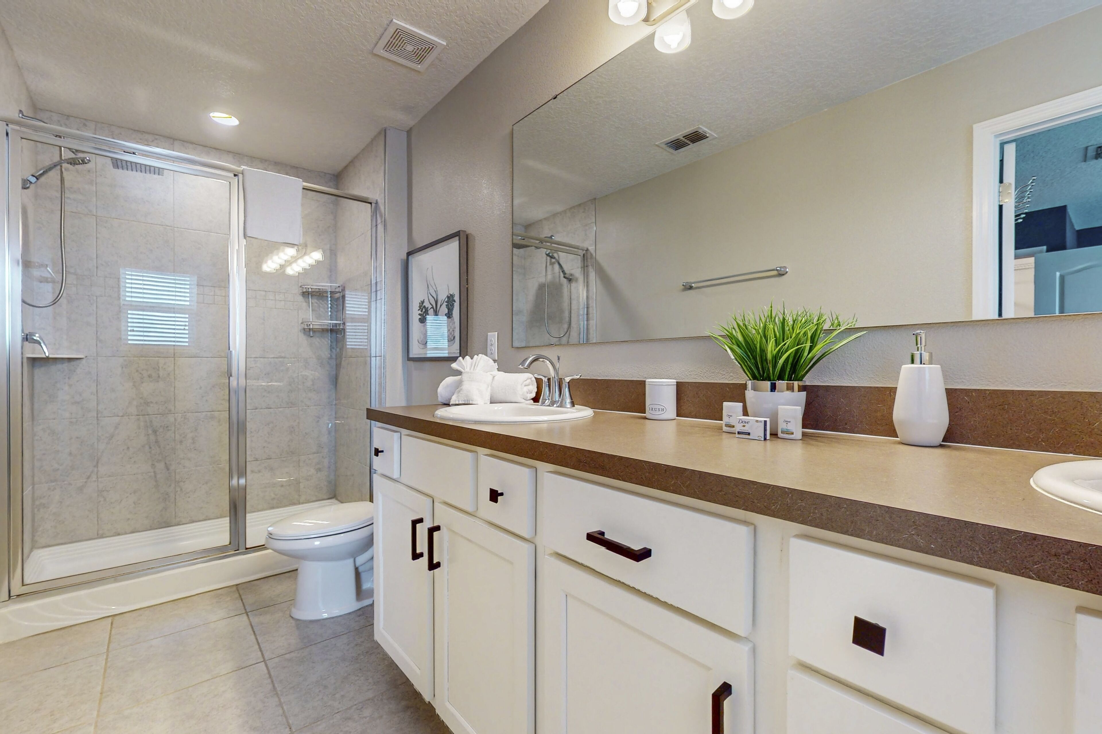 A modern bathroom with a glass-enclosed shower, a white toilet, a beige countertop, and a large mirror.