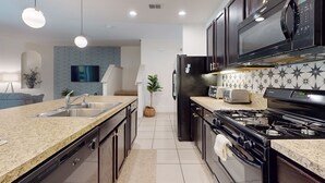 A modern kitchen with dark wooden cabinets, a granite countertop, a built-in microwave, a gas stove, and a sink. - Solterra Escape | Private Pool | Café, Tennis & Water Park with Lazy River (Davenport)