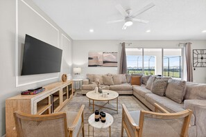 A modern living room with a large flat-screen TV, a sectional sofa, a coffee table, and a ceiling fan. - Exquisite home with pool, lanai, game room, central AC, & washer/dryer (Davenport)