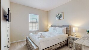 Ein Schlafzimmer mit einem hölzernen Bettgestell, einem an der Wand befestigten Fernseher, einem Fenster mit Jalousien und einem Nachttisch mit Lampe.