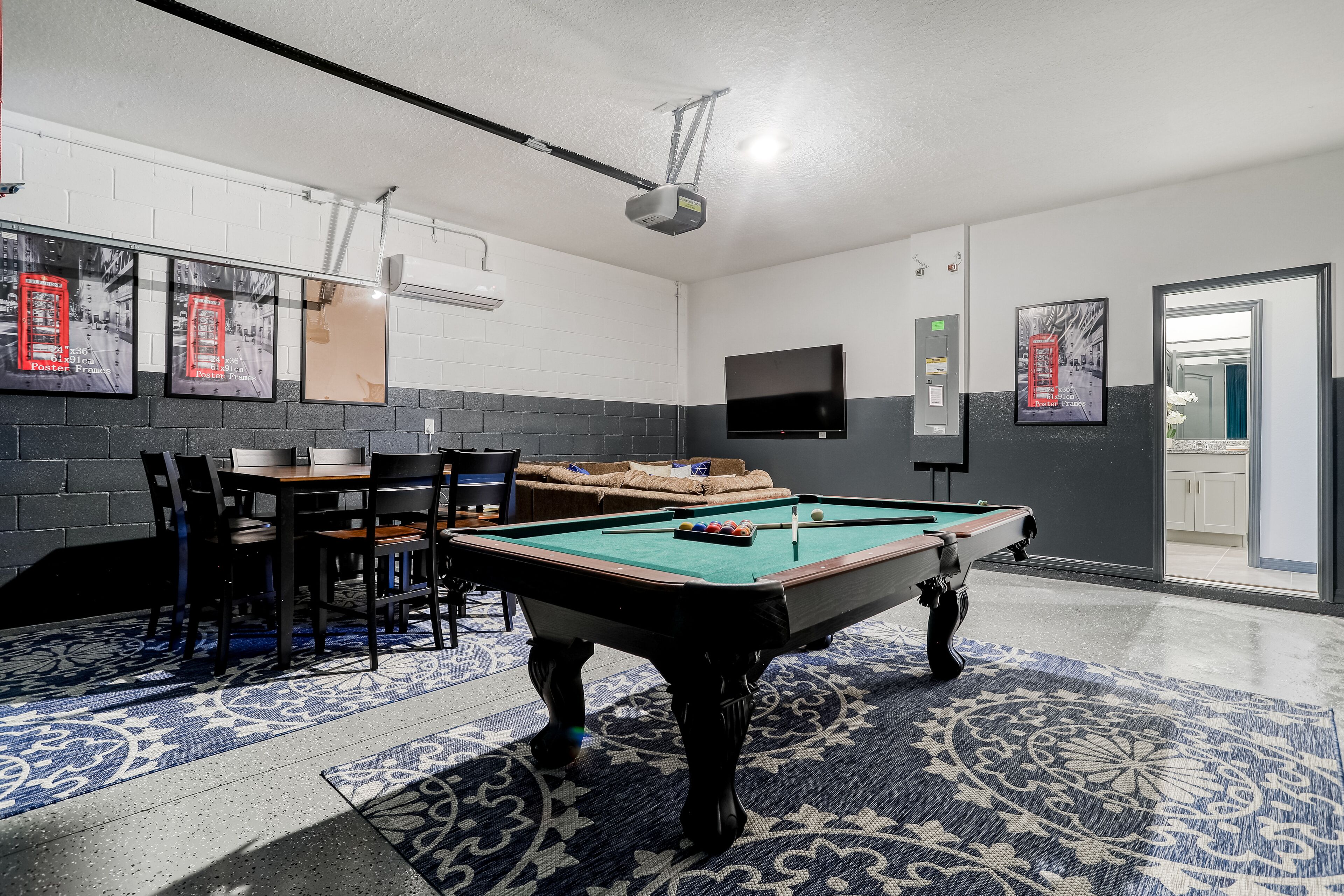 A pool table in a room with a patterned carpet, a sofa, and a television mounted on the wall.