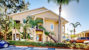 A multi-story hotel with a beige exterior, a covered outdoor area, and a parking lot with several cars. - Sunny condo with pool, hot tub, tennis court, & gym - balcony & washer/dryer (Kissimmee)