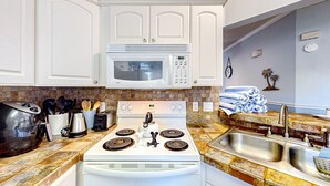 A kitchen with white cabinets, a microwave, a stove, a sink, and various kitchen appliances. - Sunny condo with pool, hot tub, tennis court, & gym - balcony & washer/dryer (Kissimmee)