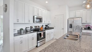 A modern kitchen with white cabinets, stainless steel appliances, and a granite countertop. - Modern Family Home - Private Pool, Lanai, WiFi, Central AC & Washer-Dryer (Davenport)