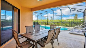 A covered patio with a dining table and chairs, a ceiling fan, and a view of a swimming pool. - Modern Family Home - Private Pool, Lanai, WiFi, Central AC & Washer-Dryer (Davenport)