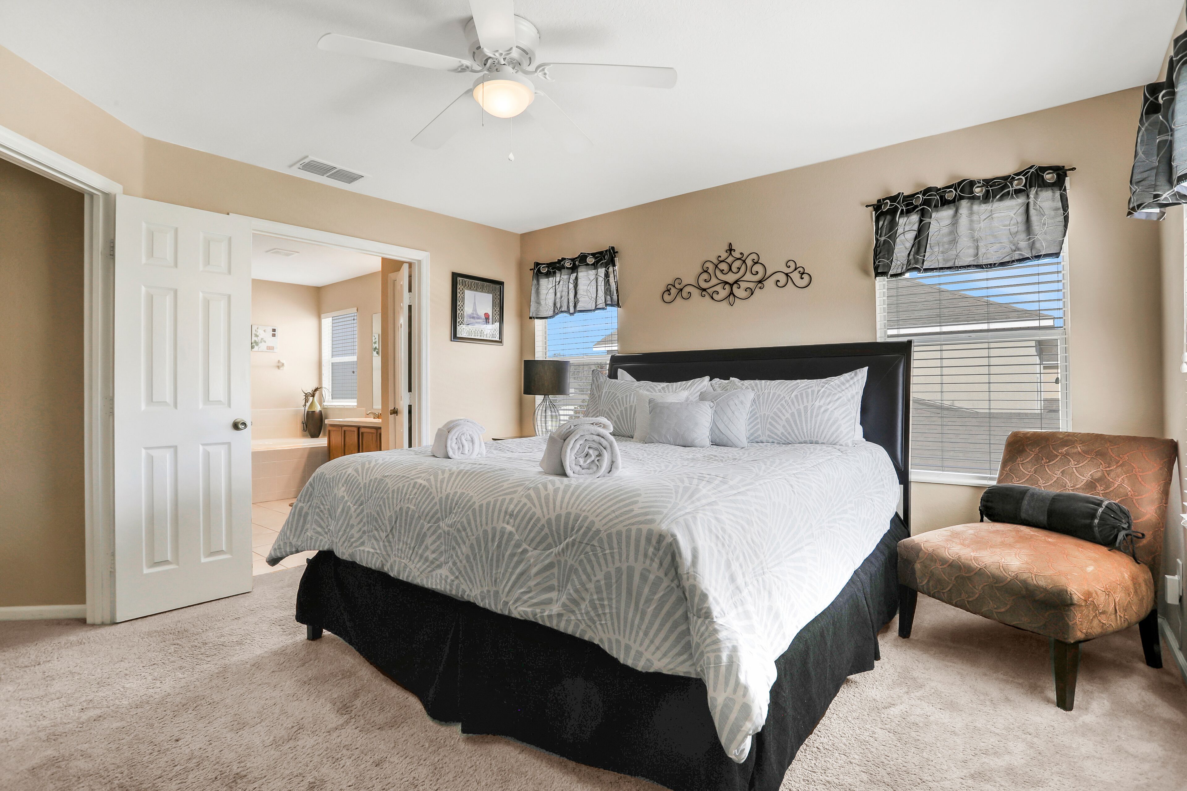 A bedroom with a bed, a chair, a ceiling fan, a window with blinds, and a door.
